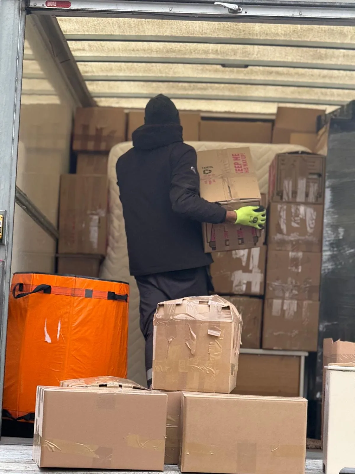 Crew carrying boxes into a modern brick house with a Luton van on the drive